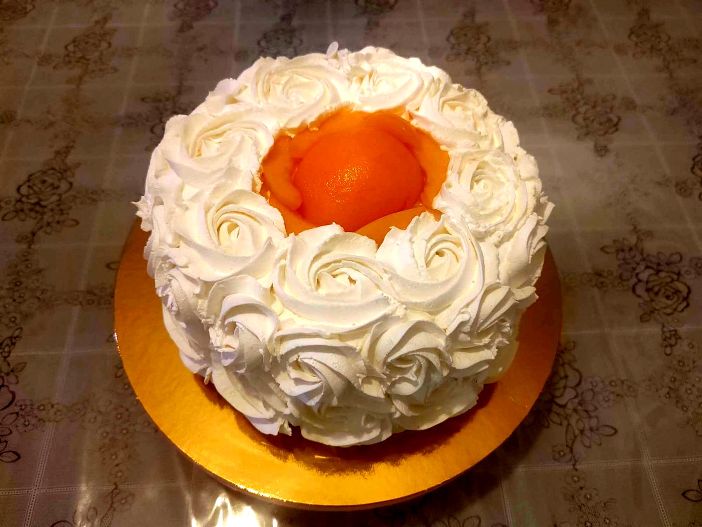 Tarta cubierta de rosetones de crema blanca con melocotón en el centro